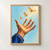 An open terracotta-toned hand in a blue sleeve reaches upward beneath three golden moths against a pale blue background.; frame shown for styling only