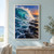 A turquoise ocean wave curls into white spray against dark jagged rock shelves beneath a warm sunset horizon.; frame shown for styling only
