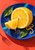 Bright sliced lemon and separated wedge on a cobalt-blue plate with leaves, droplets and curled zest against a coral tabletop.