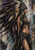 Right-facing woman wearing an oversized feather headdress, bead ornaments, and a jeweled belt against a distressed abstract background.