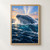 Blue whale surfacing through white spray above deep blue ocean water, with an apricot band of light on the horizon.; frame shown for styling only