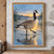 Canada goose stepping through shallow water with one foot lifted, framed by reeds and golden dawn reflections.; frame shown for styling only
