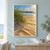 Dune grasses bend across sunlit sand beside ocean surf and teal-blue water beneath a bright sky.; frame shown for styling only