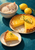 Cream kitten asleep in a blue-striped bowl beside a golden lemon tart and plated slice, with lemons and thyme on a deep teal surface.