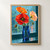 Scarlet, orange, and pale apricot poppy-like flowers and buds in a cobalt-blue glass vase before a rain-speckled turquoise window.; frame shown for styling only