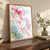 Translucent rose-pink bow and looping ribbon tails surround a small diamond-shaped kite, blue flowers, and greenery on a pale background.; frame shown for styling only
