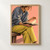 Close portrait of a seated adult in a blue-gray sweater and striped yellow trousers holding an open book and lifting a page against a coral background.; frame shown for styling only