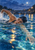 Capped swimmer turning to breathe during freestyle, with one arm underwater, the other raised with droplets, and warm lamp reflections on blue water.