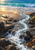 A foaming rocky stream flows over dark stones across a sandy beach toward turquoise ocean surf.