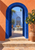 Open cobalt-blue arched doors in a terracotta wall reveal a tiled fountain and potted lemon tree in a sunlit courtyard.