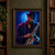 An adult saxophonist in a dark suit and wide-brimmed hat bows his head over a reflective saxophone against blue and magenta light.; frame shown for styling only