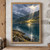 A mountain lake beneath cloudy ridges, with sunlight illuminating a golden shore and reflecting on the water beside a rocky foreground bank.; frame shown for styling only