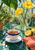Cobalt-rimmed teacup and saucer beside lemons and coral cloth, with yellow flowers in a clear pitcher on a green tiled table.