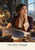 Adult woman astronomer at a desk holding brass dividers above a star chart, with an armillary sphere, books, window and “One More Thought” lettering.