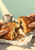 Hands pull apart a flaky chocolate-filled pastry above crumpled paper, with espresso and saucer in the background.