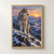 Gray wolf on a snowy rocky ridge looking toward a peach-and-gold sunrise over layered blue mountains.; frame shown for styling only