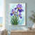 Three violet iris blooms and an unopened bud rise among long green leaves with bright droplets against a pale aqua background.; frame shown for styling only