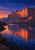 A coral-orange sandstone escarpment reflected in a calm blue desert lake, with foreground reeds beneath an indigo sky.