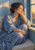 Adult woman in a blue robe sits on a cushioned window seat, resting her cheek in one hand beside a sunlit window.