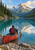 Adult paddler seen from behind in a red canoe on a reflective mountain lake, with forested slopes and a snow-dusted peak.