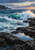 Turquoise breaking wave with white spray meeting a dark rocky shoreline, with a reflective tide pool in the foreground and headland at left.