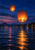 Two glowing orange paper lanterns above a reflective river at dusk, with shoreline lights and dark hills in the distance.