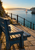Weathered blue wooden bench beside harbor steps and railing, with calm water, a small sailboat, and distant headlands.