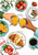 Two hands clink orange-juice glasses above a brunch spread with fruit, croissant, yogurt, coffee, and flowers.
