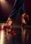Dancer’s lower legs in navy trousers wearing polished ruby-red strappy heels, one planted and one raised onto its toe on a reflective dark floor.