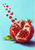 Opened crimson pomegranate with pale membrane and seeds rising in an arc on a turquoise ground beside a green leaf.