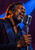 Close portrait of a dark-skinned blues singer with eyes closed beside a silver microphone against cobalt and plum lighting.