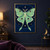 Pale mint-green moth with purple-and-gold eyespots and long tails centered among gold stars on a deep blue field.; frame shown for styling only