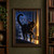 A black cat with an arched tail lifts a paw toward a glowing moth on a rainy windowsill, with an indigo city skyline and amber light behind it.; frame shown for styling only