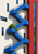 Cobalt-blue exterior stair zigzagging across a white modern facade beside a red vertical section and planted landing.