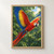 Scarlet macaw flying across a leafy green canopy, wings extended and long red-and-blue tail trailing toward the lower left.; frame shown for styling only