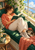 An adult woman reads an open book on a deep green window seat while a cat sleeps nearby in a sunlit room.