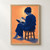 Adult with gathered hair reading an open book while seated sideways on a wooden stool against an apricot-orange background.; frame shown for styling only