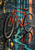 A vermilion bicycle leans against a dark curb on a wet urban street with turquoise and coral reflections and a yellow leaf.