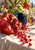 Split pomegranate and spilled seeds on pale linen beside a tipped blue bowl, leafy branch, whole fruit, and glass carafe.
