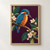 Blue-and-rust kingfisher perched on a flowering branch with its bill aimed toward a pale pink blossom against a plum background.; frame shown for styling only