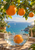 Three oranges hang from a flowering leafy branch above a glass bowl splashing with an orange, with turquoise sea beyond.