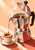 An open stainless-steel moka pot pours a thin stream of coffee into an espresso cup and saucer against a pale peach background.