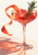 Ruby-pink grapefruit-style drink in a broad faceted coupe, with curling grapefruit peel, rosemary, bubbles, and a coral-lit tabletop.