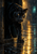 Black panther with golden eyes steps from a dark doorway onto wet stone pavement reflecting amber light.