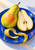 Whole yellow-green pear and seeded cut half on a vivid blue plate, with a curling peel ribbon across the foreground.