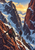Two backpacked climbers move along a snowy alpine ridge between rust-colored mountain walls toward a golden opening in the clouds.