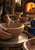 Cropped hands shape a ridged clay bowl on a pottery wheel in a warm workshop with finished bowls and a glowing kiln.