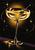 Luminous pale-gold coupe cocktail with an olive and citrus peel against a dark background with orbital lines and starbursts.