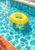 A bright yellow inflatable ring floats alone on sparkling turquoise pool water, with pale coping above and terracotta tiles at lower left.