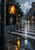 Amber pedestrian walking icon and unlit hand signal on a pole beside a rain-soaked zebra crossing with amber reflections.